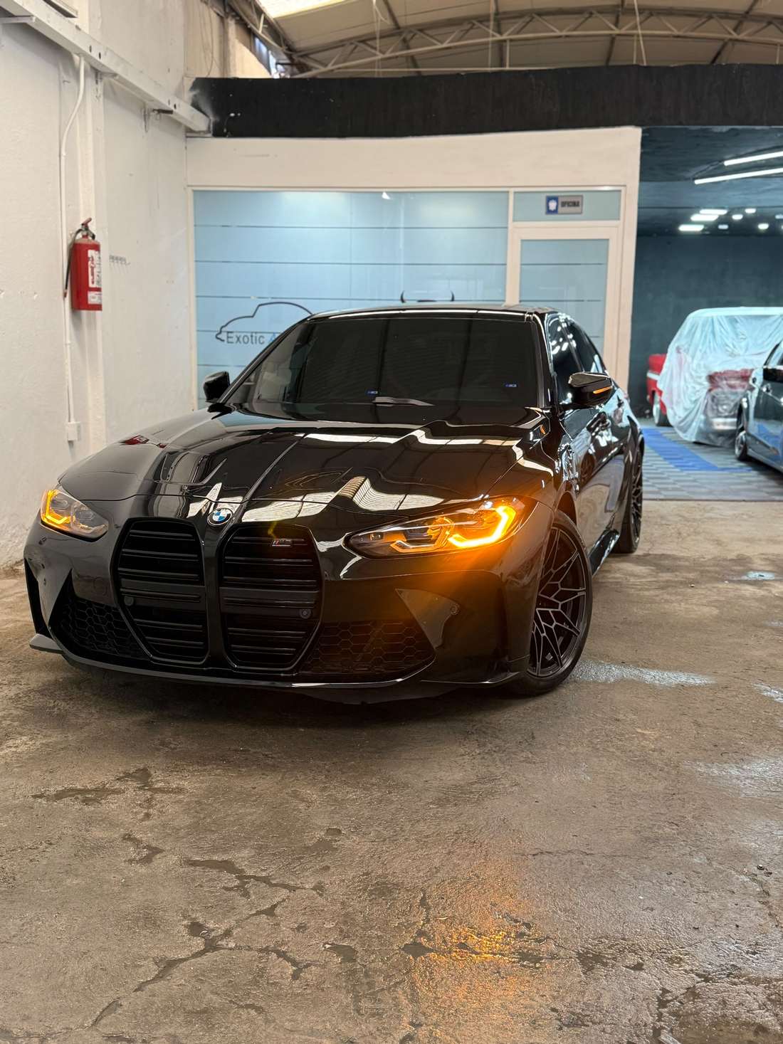 BMW M3 negro con los faros encendidos dentro del taller