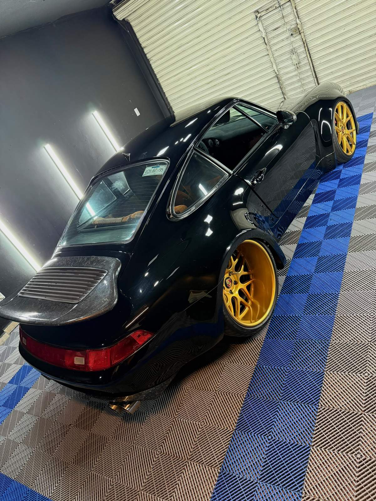 Porsche 911 993 negro con rines dorados dentro del taller