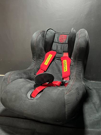 Autoasiento de bebe forrado en gamuza con arneses rojos y escudo Porsche